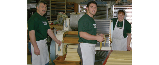 The Durante family rolling and pressing fresh pasta dough through the shop's rolling machine