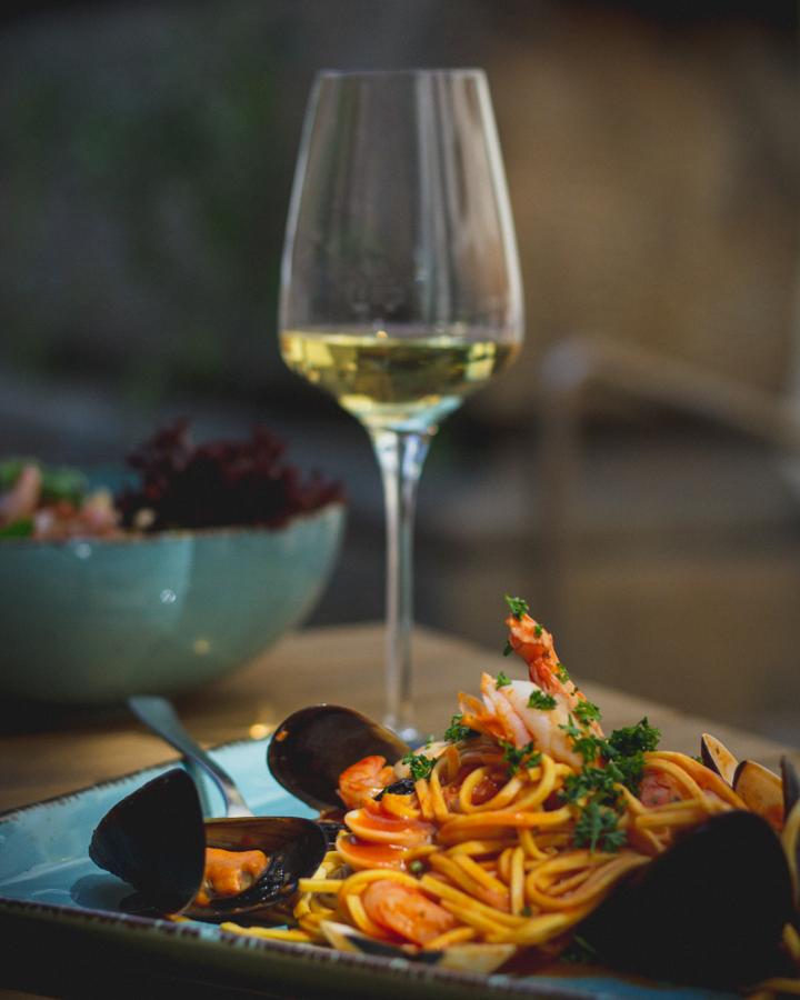 A restaurant plate of seafood linguine with mussels and shrimp, a glass of white wine behind it